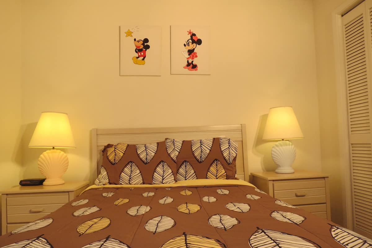 Ein Schlafzimmer mit einem Bett mit Blättermuster, zwei Wandlampen und zwei gerahmten Mickey Mouse Postern.