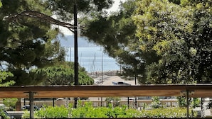 Udsigt fra en balkon over et kystområde med træer, en vej og parkerede biler.