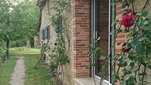 A rustic stone building with a brick section, a wooden porch, and a gravel path leading to the entrance.