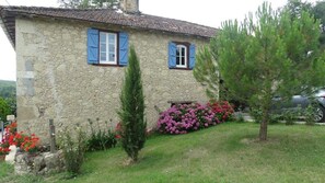 A rustic stone house with two windows, each with blue shutters. There is a small tree and flowering plants in the front yard. - Ideal for recharging (Faget-Abbatial)