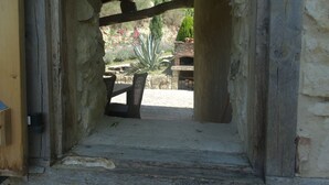 A rustic stone archway leading to an outdoor patio area with a brick oven and a variety of plants.