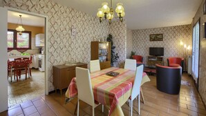 A dining area with a table set for four, a television in the background, and a kitchen visible through an open doorway.