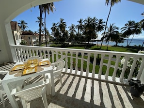 Een balkon met een tafel en stoelen, met uitzicht over een verzorgd gazon, palmbomen en de oceaan.
