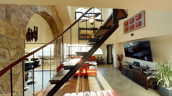 A spacious living area with a stone archway, a staircase, a large TV, and a dining area. - one block to medano beach , 2 blocks to the Cabo Marina & Downtown Cabo (Cabo San Lucas)