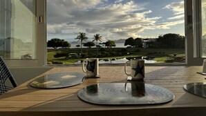 Ein Tisch mit zwei Tassen und einem Untersetzer, ein Fenster mit Blick auf eine Landschaft, die Bäume und ein Gewässer zeigt.
