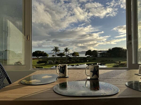 A table with two mugs and a coaster, a window with a view of a landscape including trees and a body of water. - Sapphire Beach, Crystal Cove, Your Piece of Paradise (St Thomas)