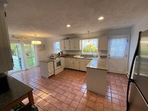 A spacious kitchen with white cabinets, a large island, and a view of the outdoors through the windows.
