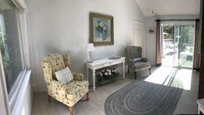 A living room with a patterned armchair, a white console table, a green vase with flowers, and a view through a glass door. - Quintessential Family Memory Cape Cod Home 1/3 walk to private association beach (East Falmouth)