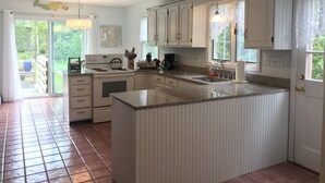 A kitchen with white cabinets, a central island, a stove, and a large window. - Quintessential Family Memory Cape Cod Home 1/3 walk to private association beach (East Falmouth)