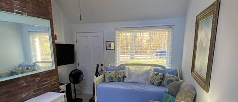 Un dormitorio con cama, ventilador de techo, televisión, ventana y espejo.