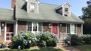 A two-story house with a red door, white windows, and a brick chimney. - Quintessential Family Memory Cape Cod Home 1/3 walk to private association beach (East Falmouth)