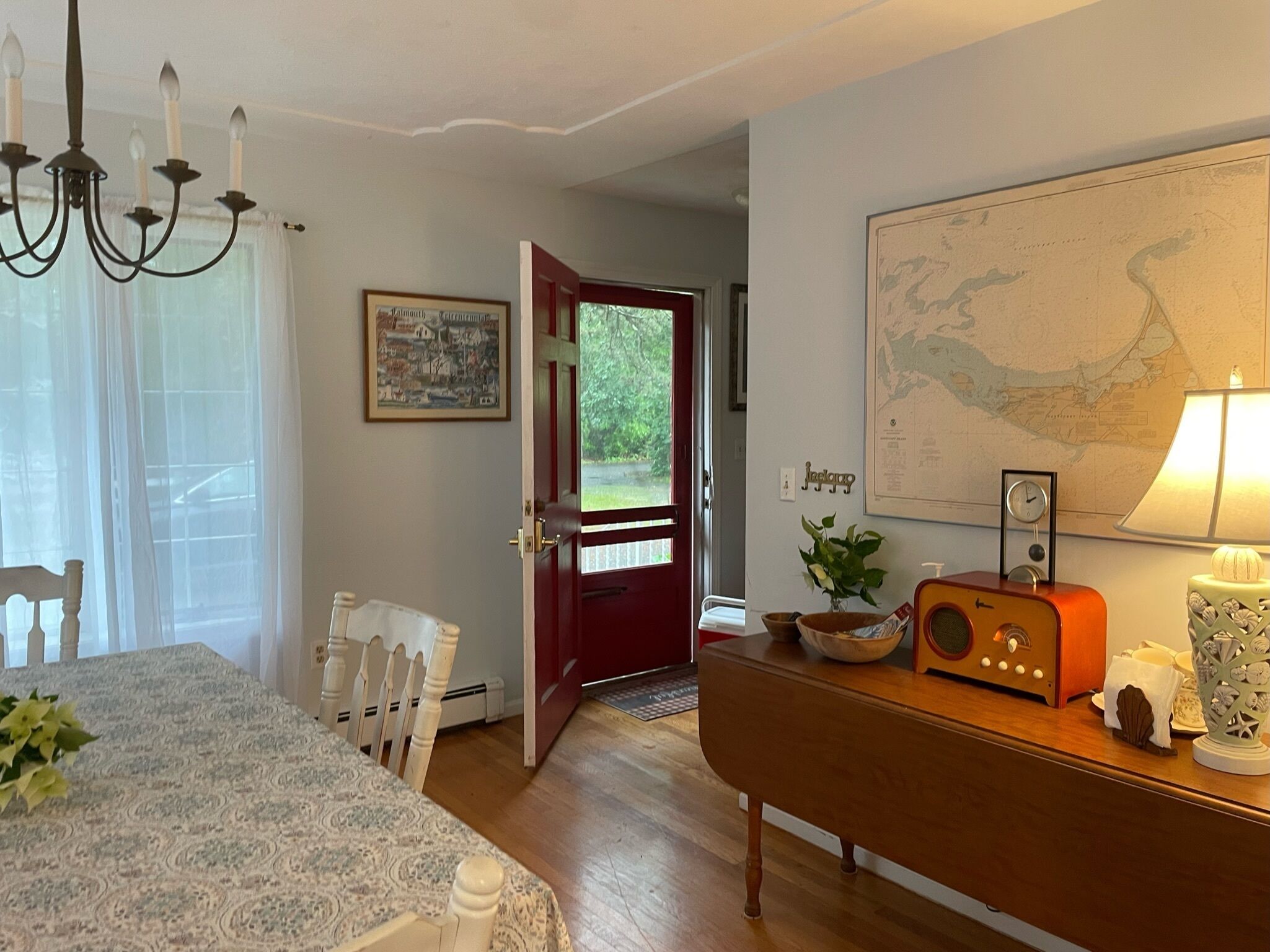 A dining area with a table set for four, a chandelier, a red door leading outside, a map on the wall, and a vintage radio.