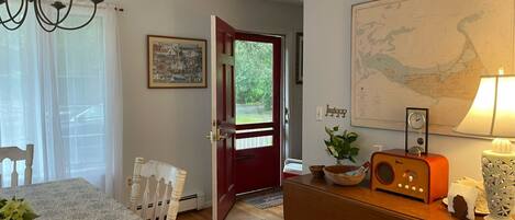 A dining area with a table set for four, a chandelier, a red door leading outside, a map on the wall, and a vintage radio.