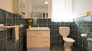 Une salle de bain moderne avec des carreaux de couleur foncée, des toilettes blanches, un lavabo avec un miroir et un porte-serviettes.