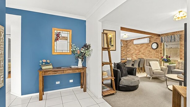 Ein modernes Wohnzimmer mit blauer Akzentwand, einem Holzkonsole und einer Sitzecke mit Sofa und Sesseln.
