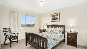 Une chambre à coucher comprenant un lit, une chaise, une table de chevet, une commode, une fenêtre avec des rideaux et un luminaire au plafond.