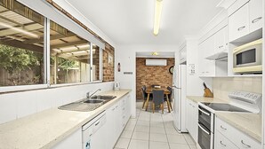 Eine kleine Küche mit weißen Schränken, einer eingebauten Mikrowelle und einem Fenster mit Blick auf einen Garten.