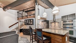A modern kitchen with a central island, bar stools, and a staircase leading to an upper level.