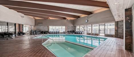 An indoor swimming pool with a tiled floor, a wooden ceiling, and a stone wall.