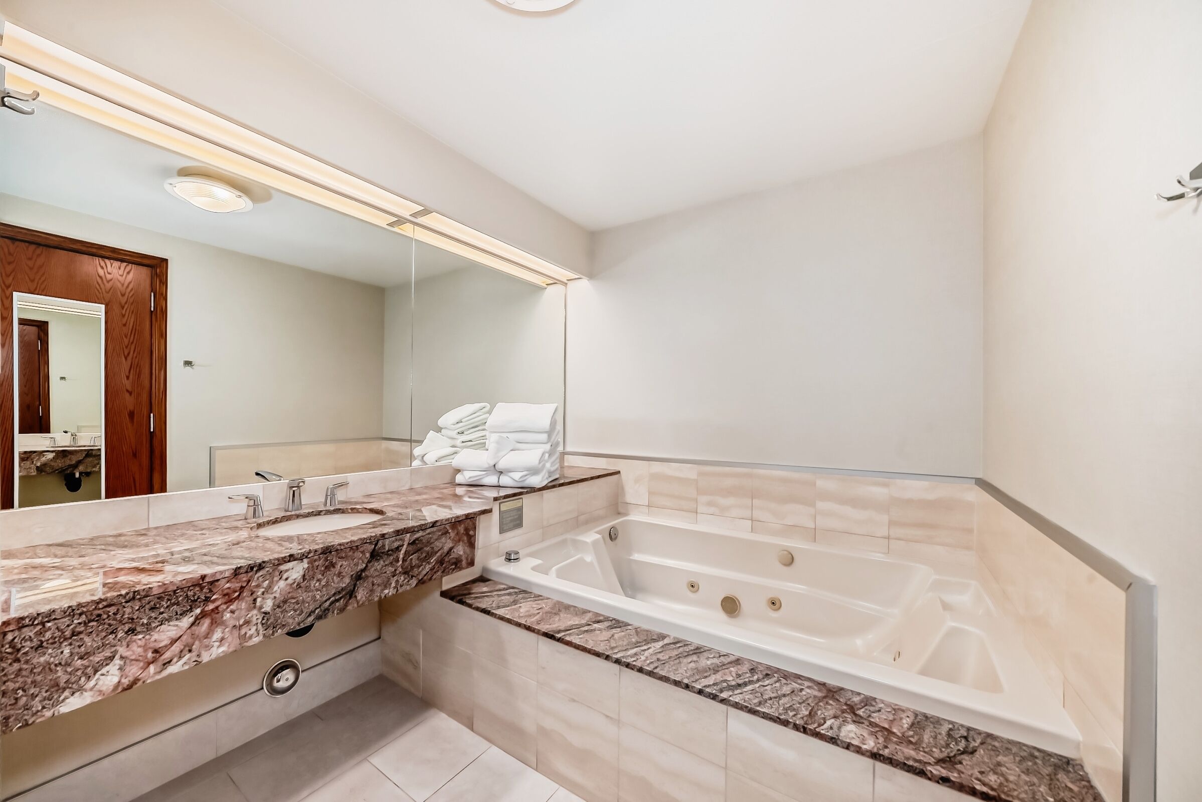 A modern bathroom with a large bathtub, a marble vanity, and a large mirror.