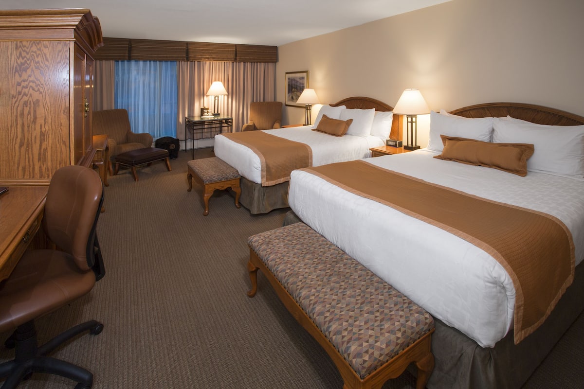 A hotel room with two beds, a desk, a chair, and a bench.