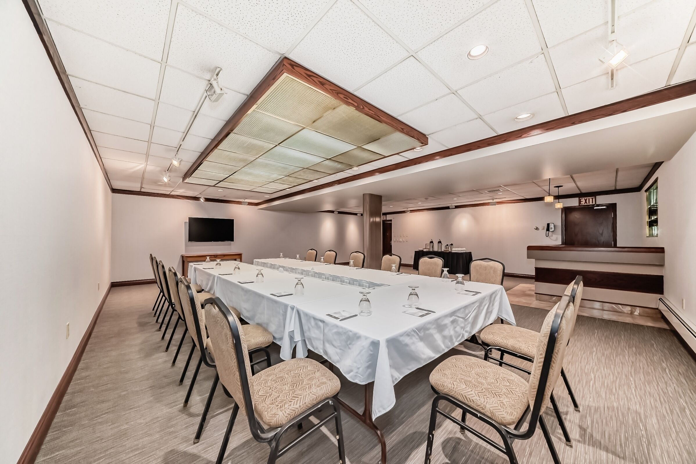 A conference room with a long table, chairs, a television, and an exit sign.