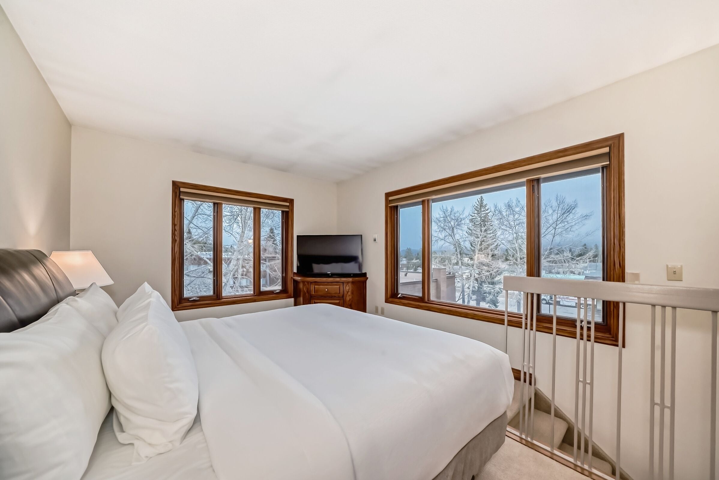 Een slaapkamer met een bed, een televisie en grote ramen met uitzicht op sneeuw.