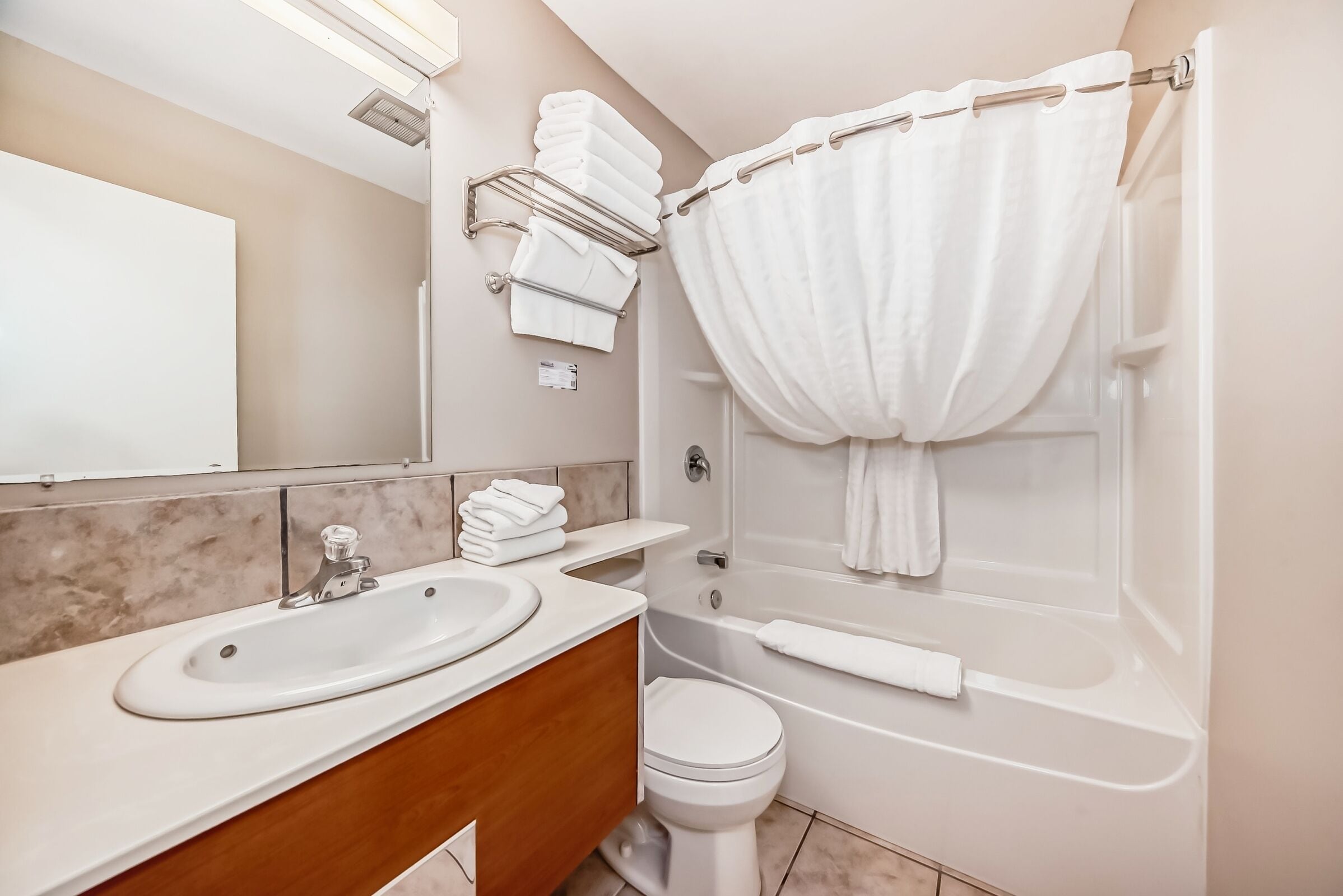 A modern bathroom with a double sink vanity, a toilet, and a bathtub with a shower curtain.
