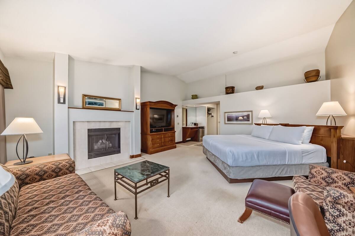 A hotel room with a large bed, a sofa, a small table, a fireplace, and a television.