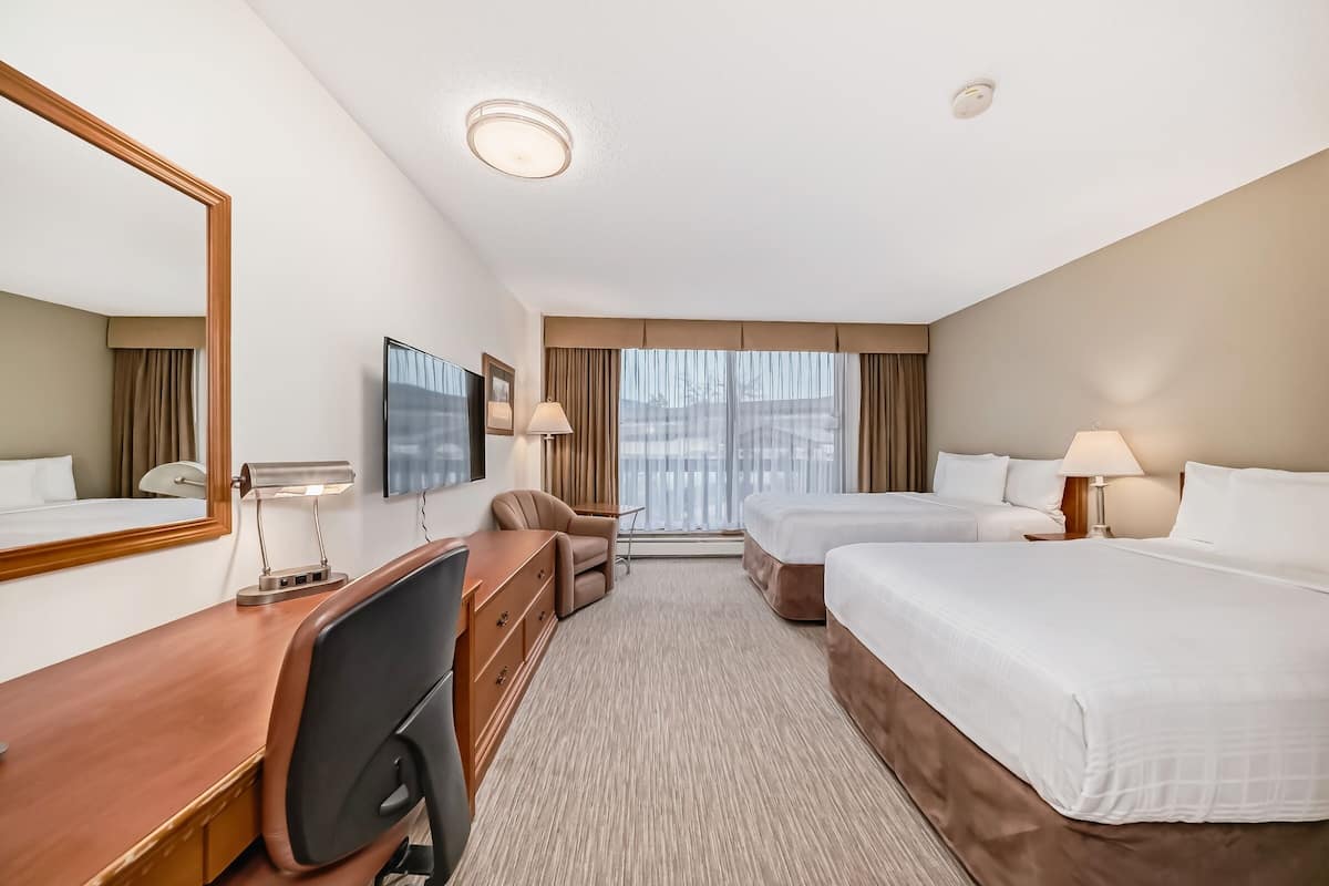 A hotel room with two beds, a desk, a chair, a TV, and a large window with curtains.