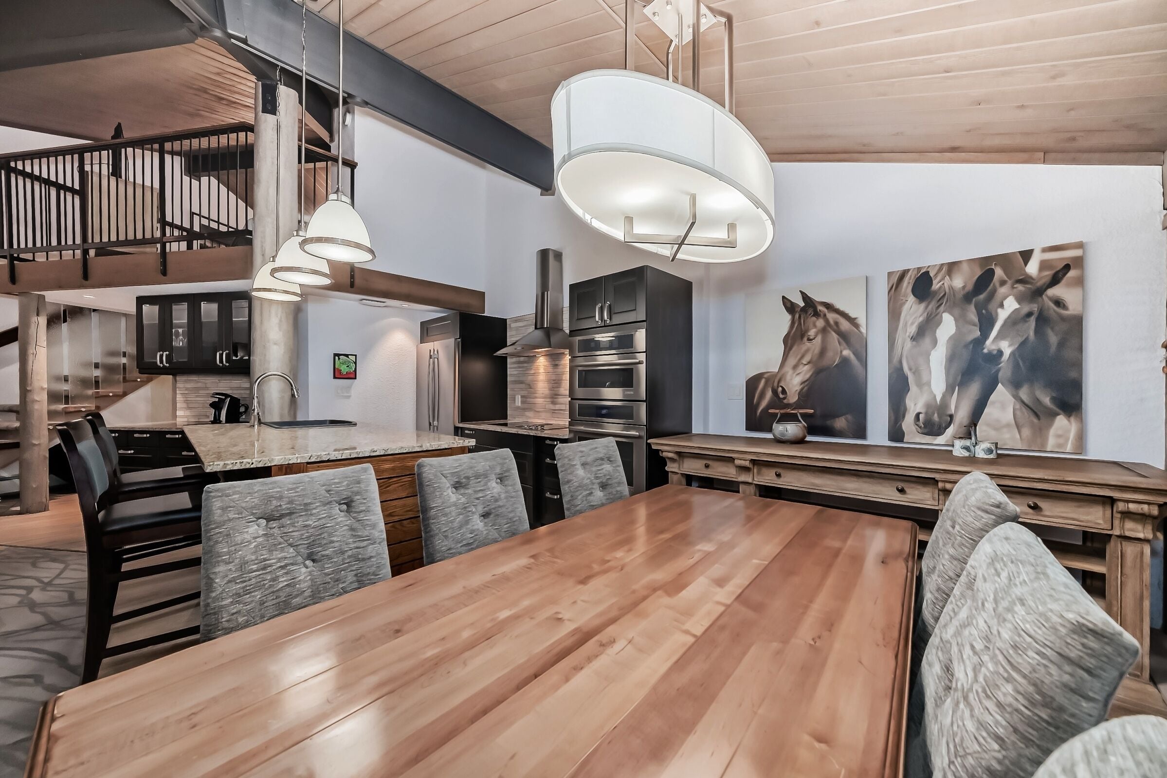 A spacious kitchen with modern appliances, a wooden dining table, and a staircase leading to an upper level.