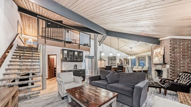 A spacious living area with a staircase leading to a loft, a kitchen, and a fireplace.