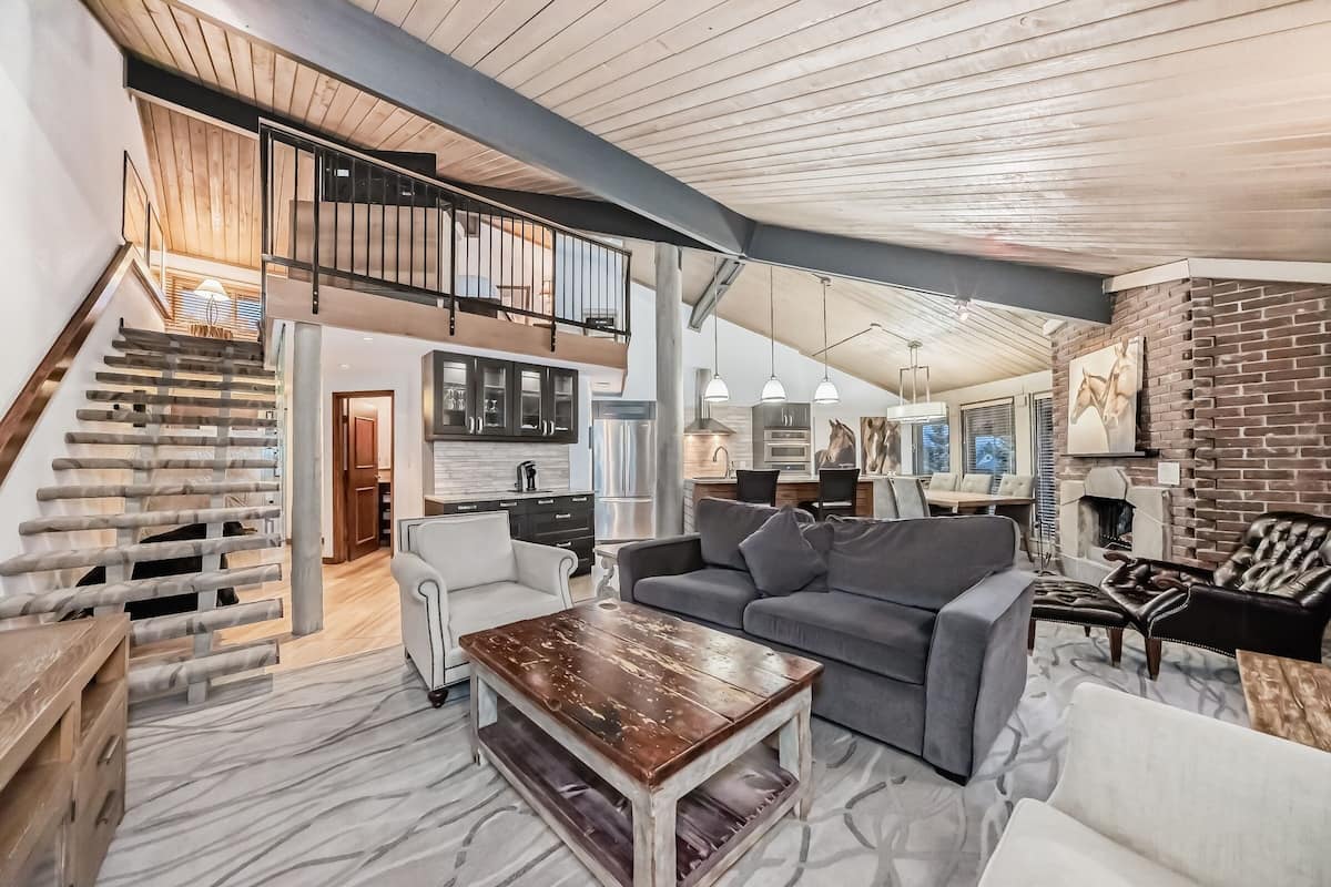 A spacious living area with a staircase leading to a loft, a kitchen, and a fireplace.