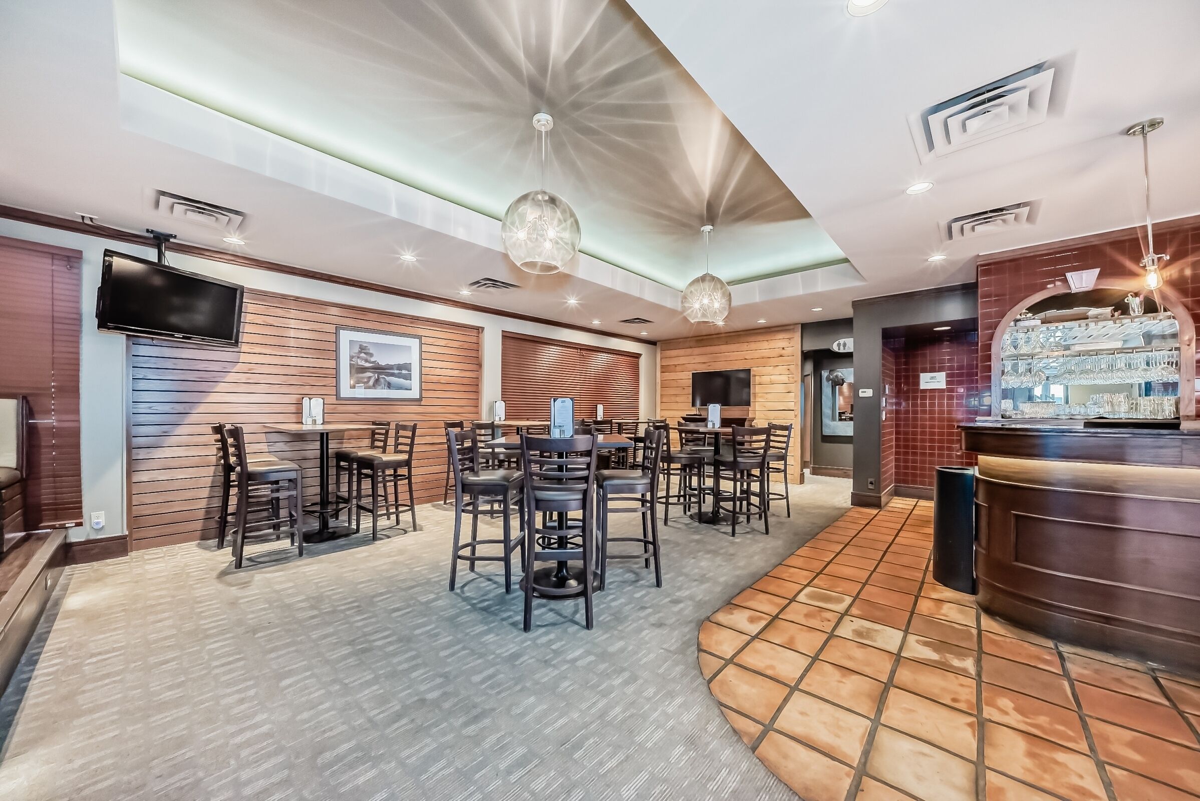 A restaurant with multiple tables and chairs, a bar area, and a television mounted on the wall.