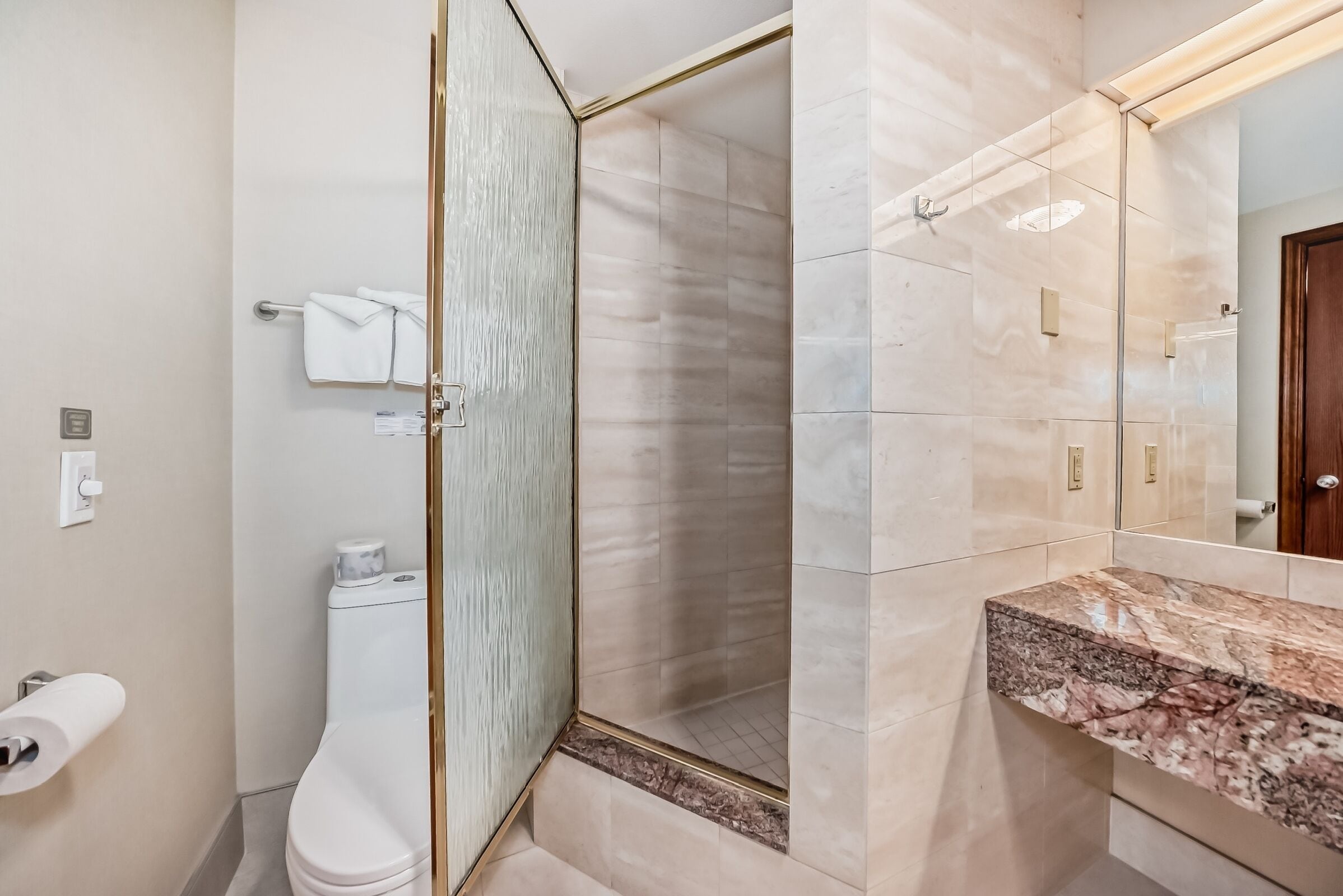 Et moderne badeværelse med brusekabine i glas, kommodevask i marmor og toilet.