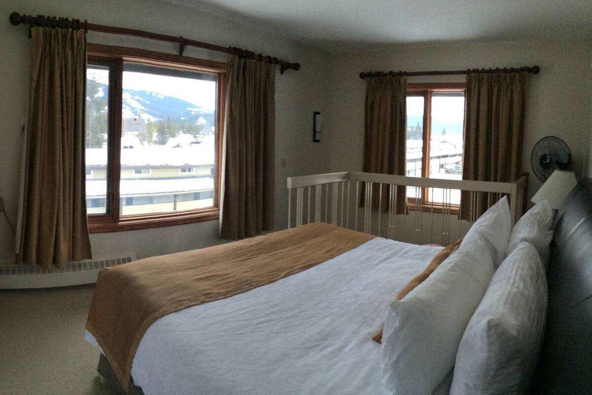 A bedroom with a bed, a dresser, a television, and windows with curtains.