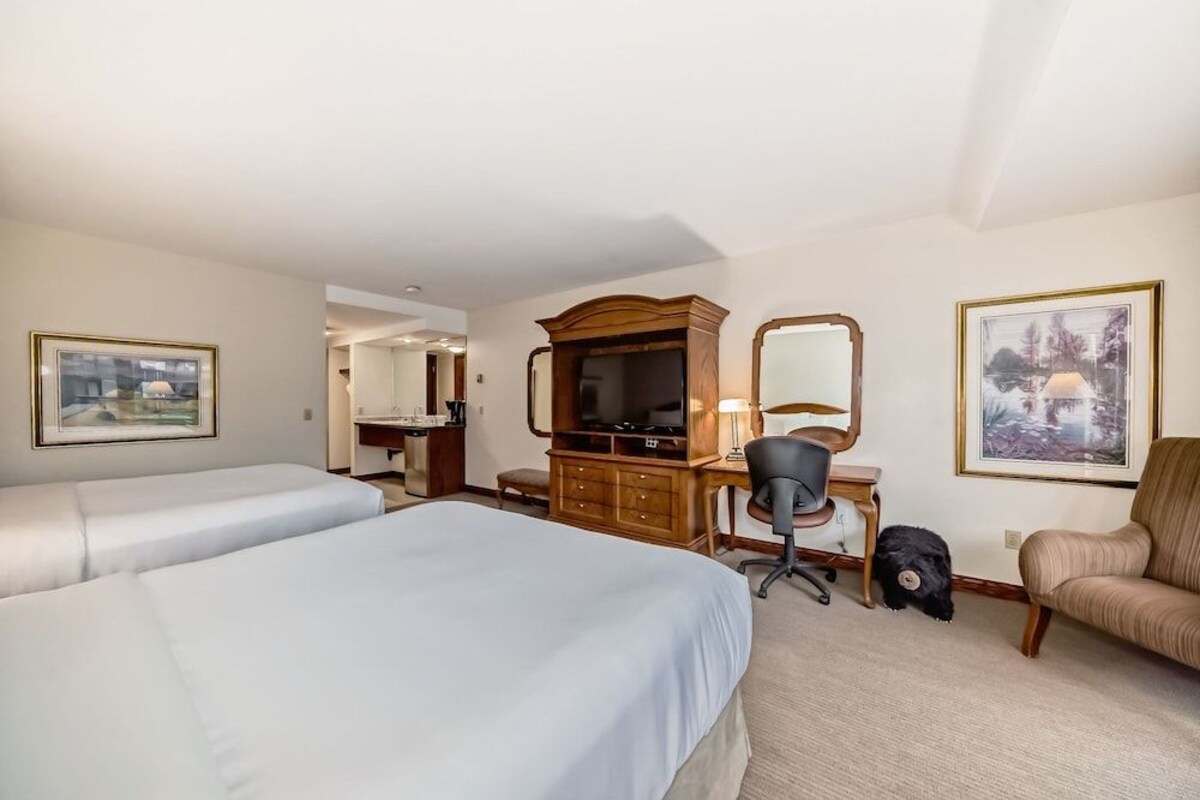 A hotel room with two beds, a desk with a computer, a chair, a dresser, and a mirror.