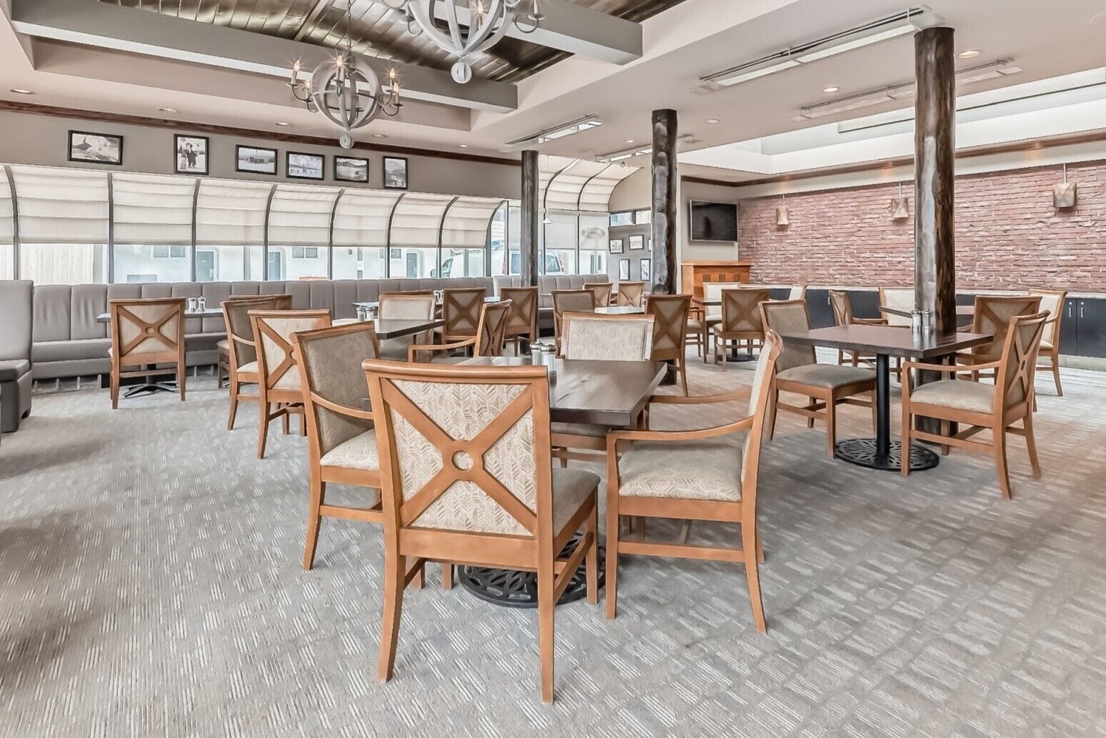A spacious dining area with wooden chairs and tables, large windows, and a brick wall.
