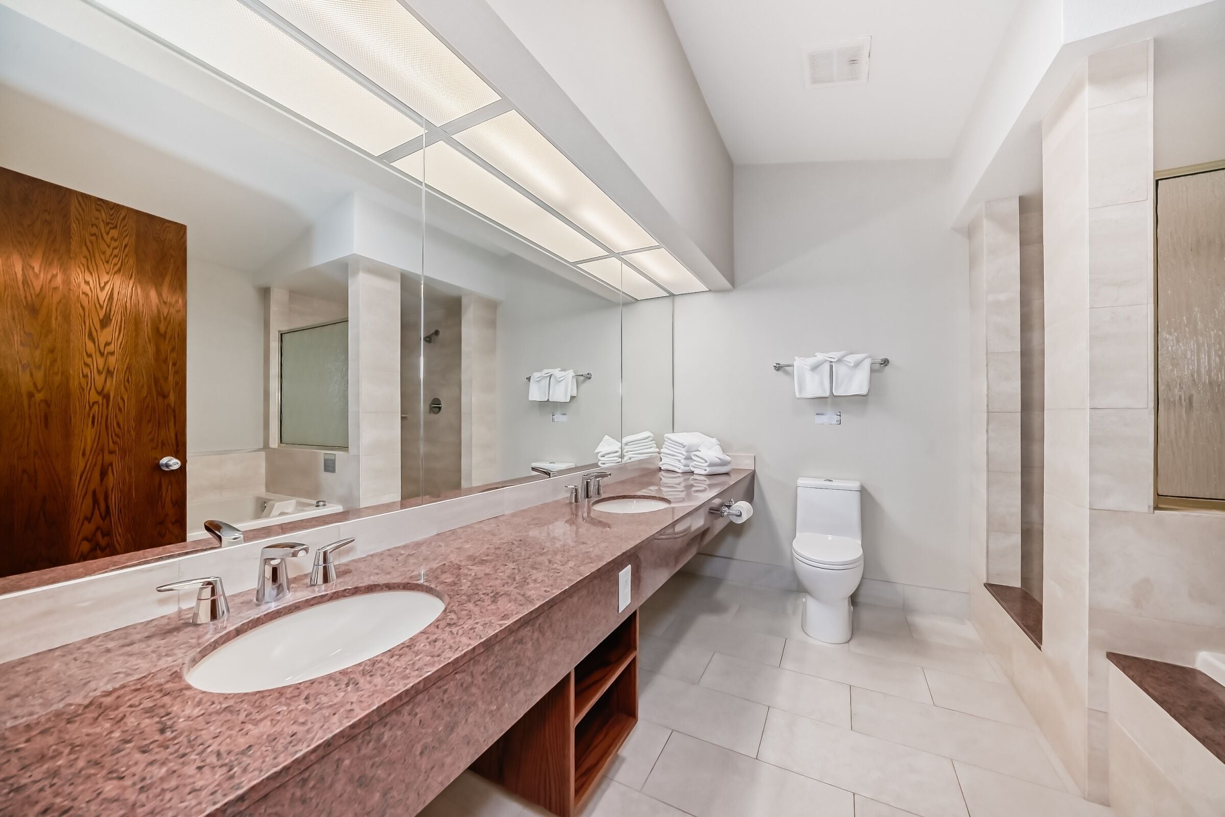 A modern bathroom with a long vanity, two sinks, a large mirror, and a toilet.