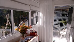 Une pièce avec un bureau, un vase de fleurs et une vue sur un balcon agrémenté d’une balustrade blanche et de plantes.