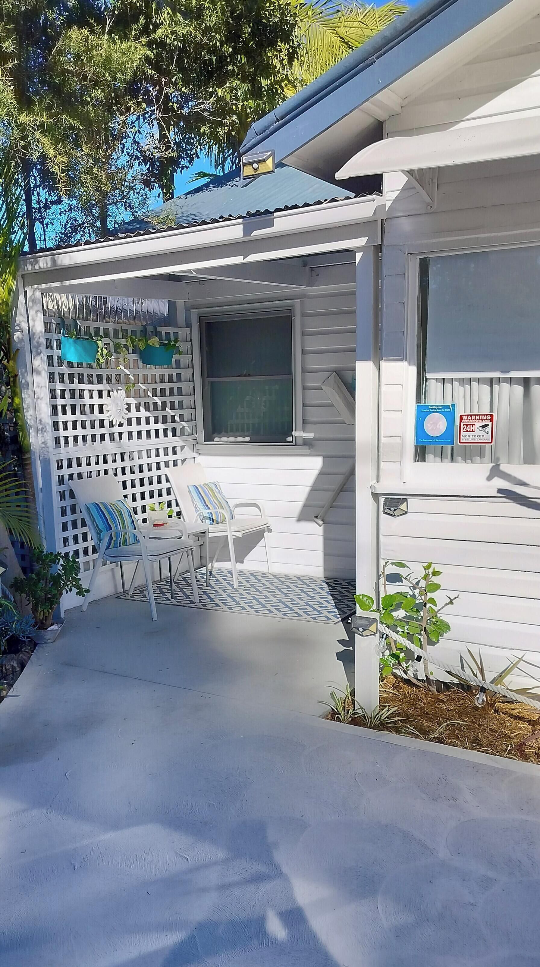 A covered outdoor seating area with a patio table and chairs, a white fence, and a window with a security sign.