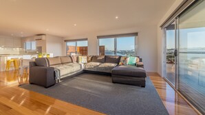 Ein modernes Wohnzimmer mit Ecksofa, Essbereich und großen Fenstern mit Blick auf Wasser und Brücke.