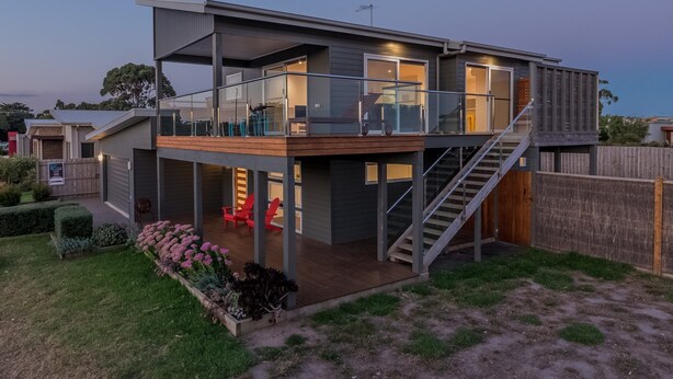 Ein modernes, zweistöckiges Haus mit Balkon, Treppe und einem umzäunten Garten.