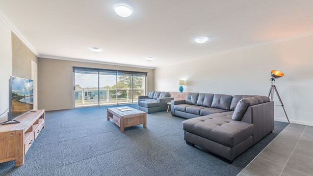 A spacious living room with a large grey sectional sofa, a wooden coffee table, a TV on a wooden stand, and a floor lamp. - Unit 4-83 Thompson Avenue, Cowes Central, includes linen. (Cowes)
