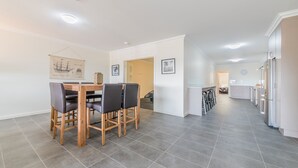 A modern kitchen with stainless steel appliances, a dining area with a wooden table and chairs, and a hallway leading to a bedroom. - Unit 4-83 Thompson Avenue, Cowes Central, includes linen. (Cowes)