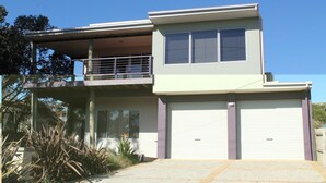 A two-story house with a balcony, large garage doors, and a small front yard with plants. - Red Rocks Road, Beach House in Cowes, bring the family! (Cowes)