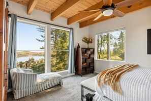Ein Schlafzimmer mit großen Fenstern, einem Deckenventilator, einem Bett, einem Sessel und einer Holzkommode.