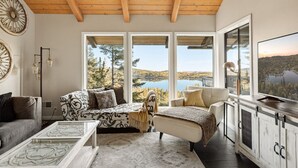 Un salon confortable avec une grande fenêtre donnant sur un lac, une cheminée et un téléviseur.