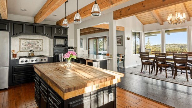 Une cuisine moderne avec un îlot central en bois, des meubles de rangement noirs et une vue sur la salle à manger.