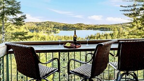 Un balcon avec des fauteuils en osier, une table et une bouteille de vin, donnant sur un lac et une forêt.